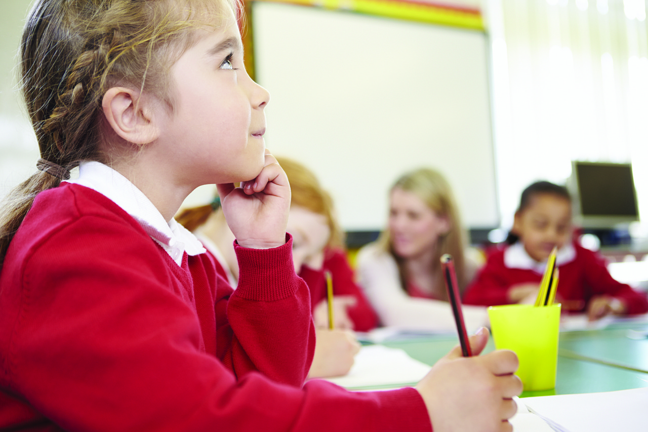 Young girl listening to someone or something out of the picture while writing something down in a class.